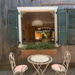 Cozy outdoor cafe seating with vintage accents, overlooking a rustic window view on a sunny day.