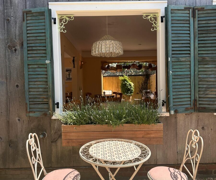 Cozy outdoor cafe seating with vintage accents, overlooking a rustic window view on a sunny day.