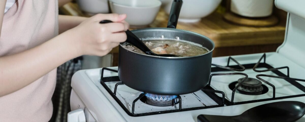 Close-up of a woman stirring soup on a gas stove in a home kitchen.
