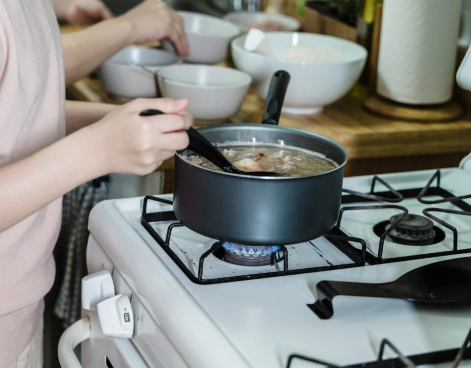 Close-up of a woman stirring soup on a gas stove in a home kitchen.